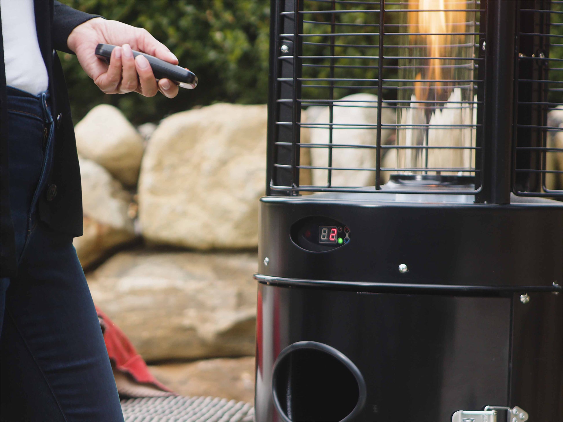 Close up of Illume Patio Heater in Black with digital control panel. Model is nearby with remote control.