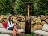 Woman seated on outdoor couch in front of Shine Patio Heater with visible Flame.