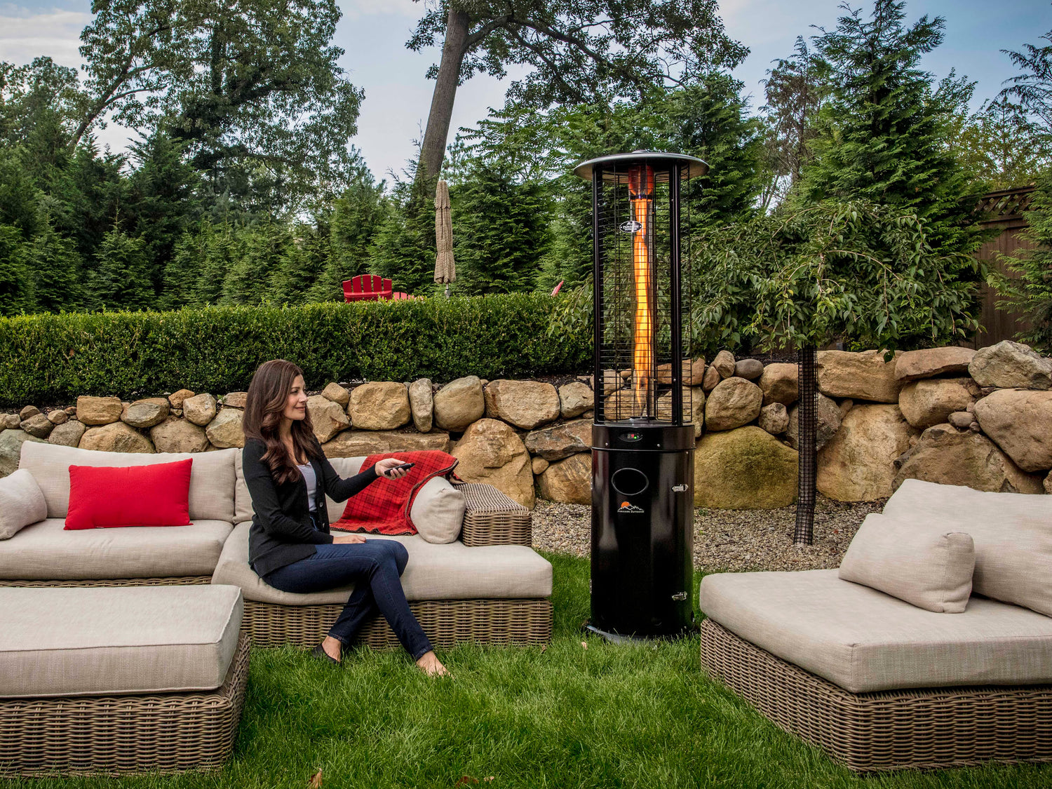 Woman sitting on outdoor furniture, pointing remote control at Illume Propane Patio Heater