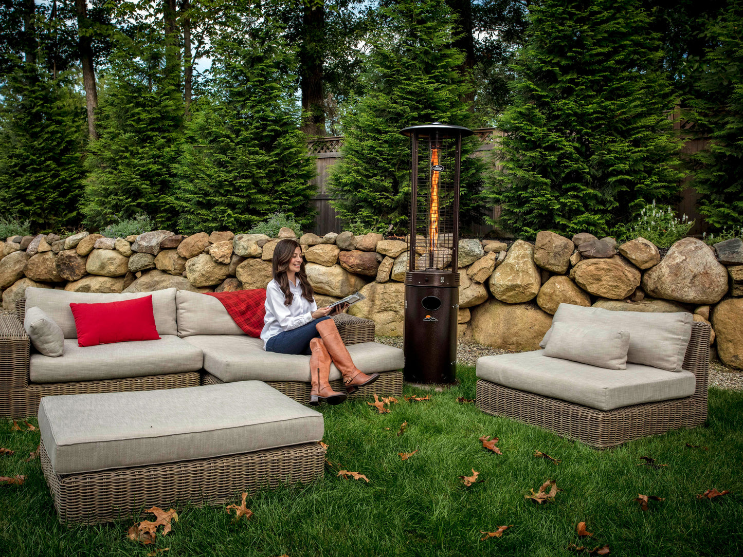 Woman seated on outdoor couch in front of Shine Patio Heater with visible Flame.