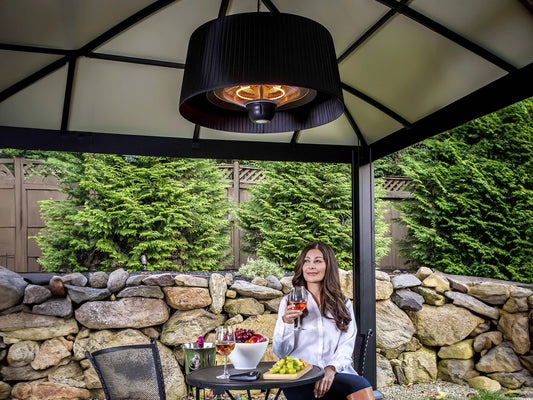 Glow Pendent Heat Lamp hanging from gazebo. Woman sitting underneath with glass of wine.