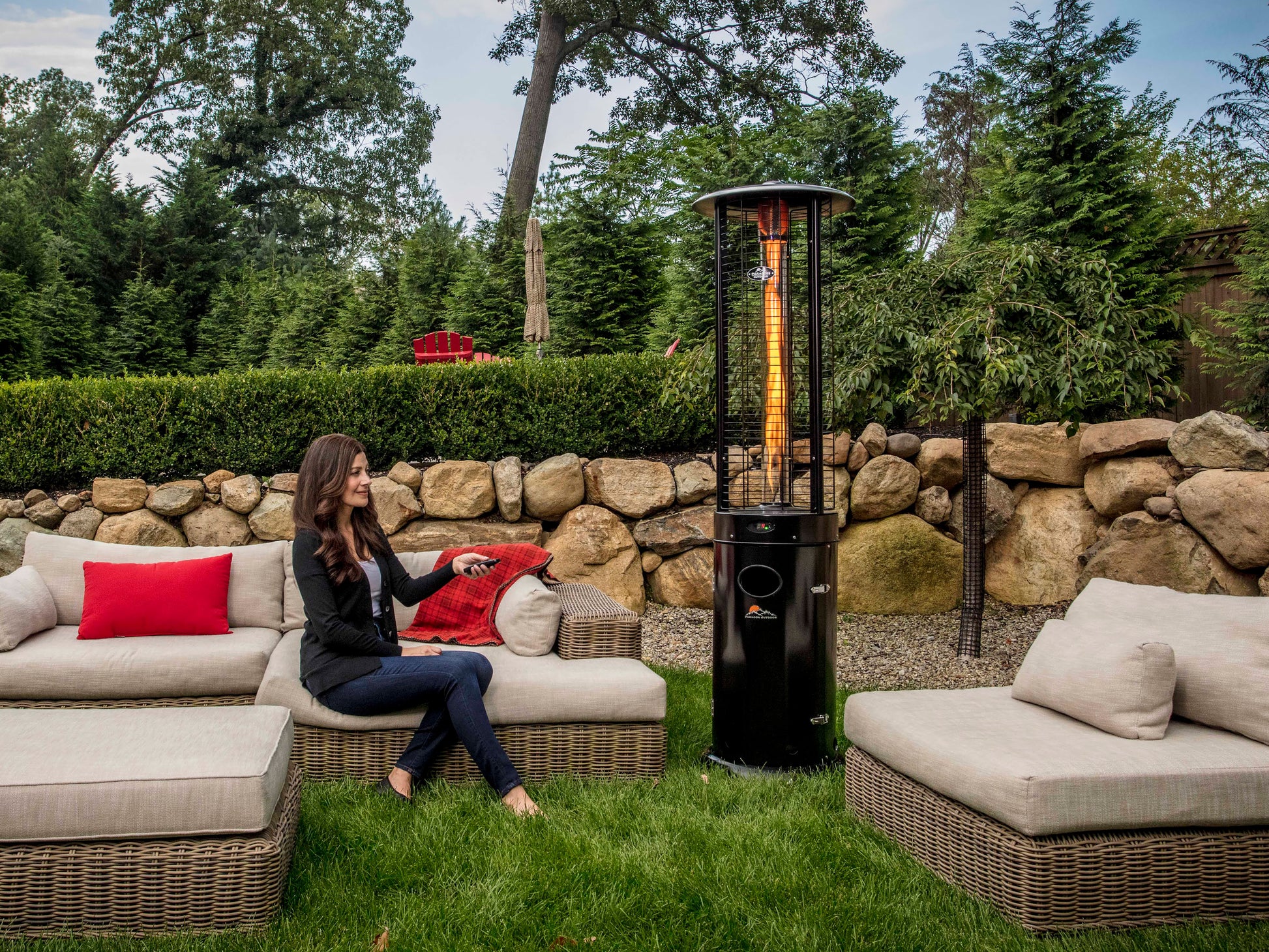 Woman sitting on outdoor furniture, pointing remote control at  Illume Propane Patio Heater