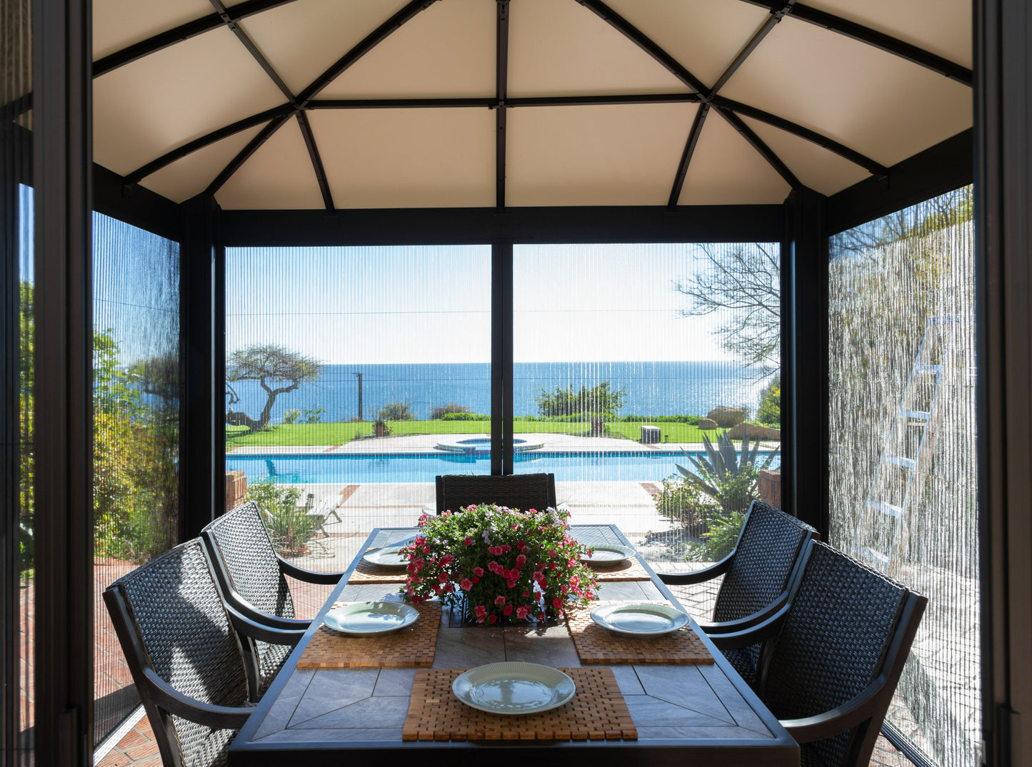 Interior of Siena Hard Top Gazebo with a set dining table overlooking pool.