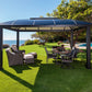 Cambridge 12' x 16' Hard Top Gazebo on grass, in front of pool with outdoor furniture underneath.
